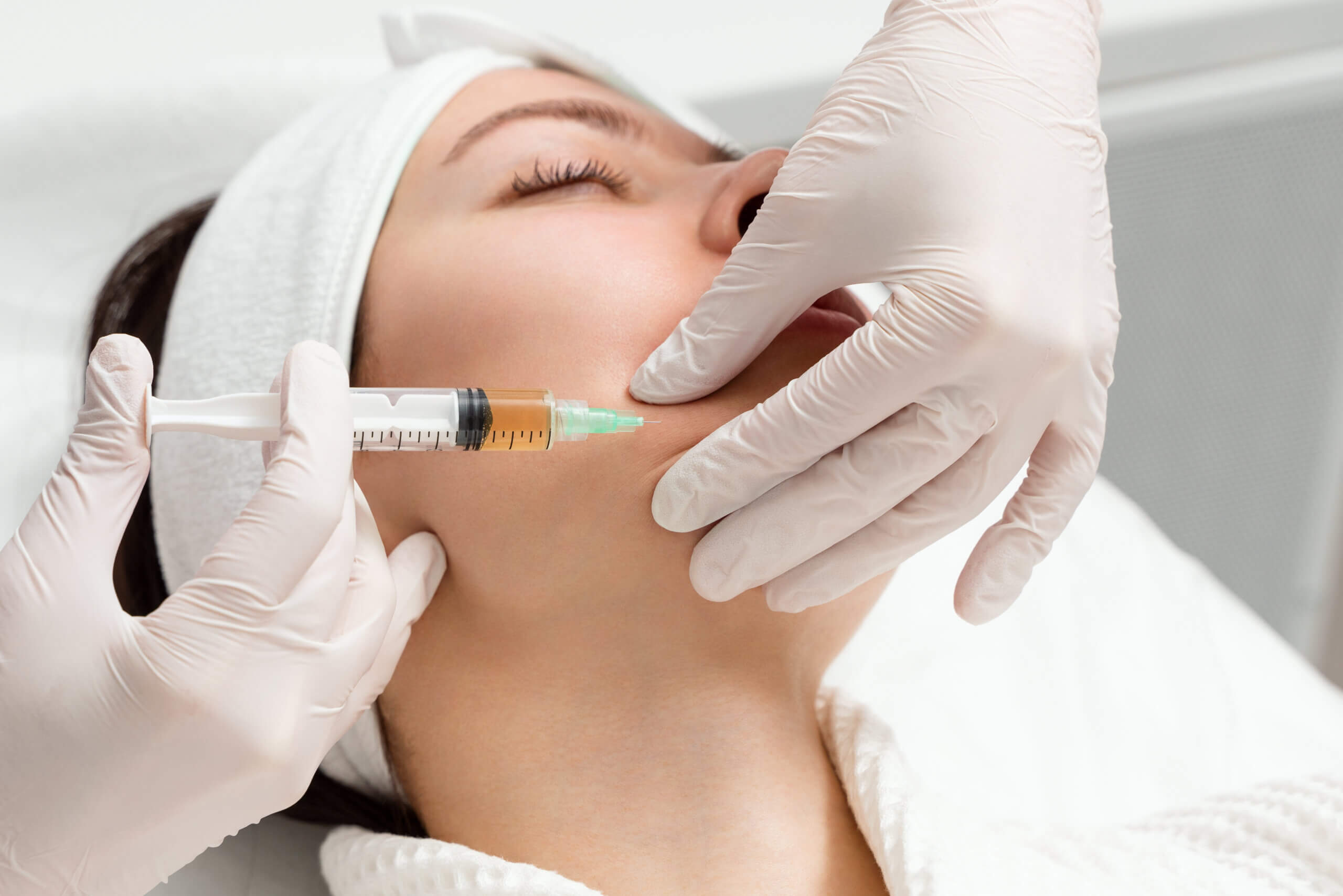 cosmetologist gives an injection into the cheekbones of a young woman.. doctor injecting hyaluronic acid into the ching of a woman as a facial rejuvenation treatment.
